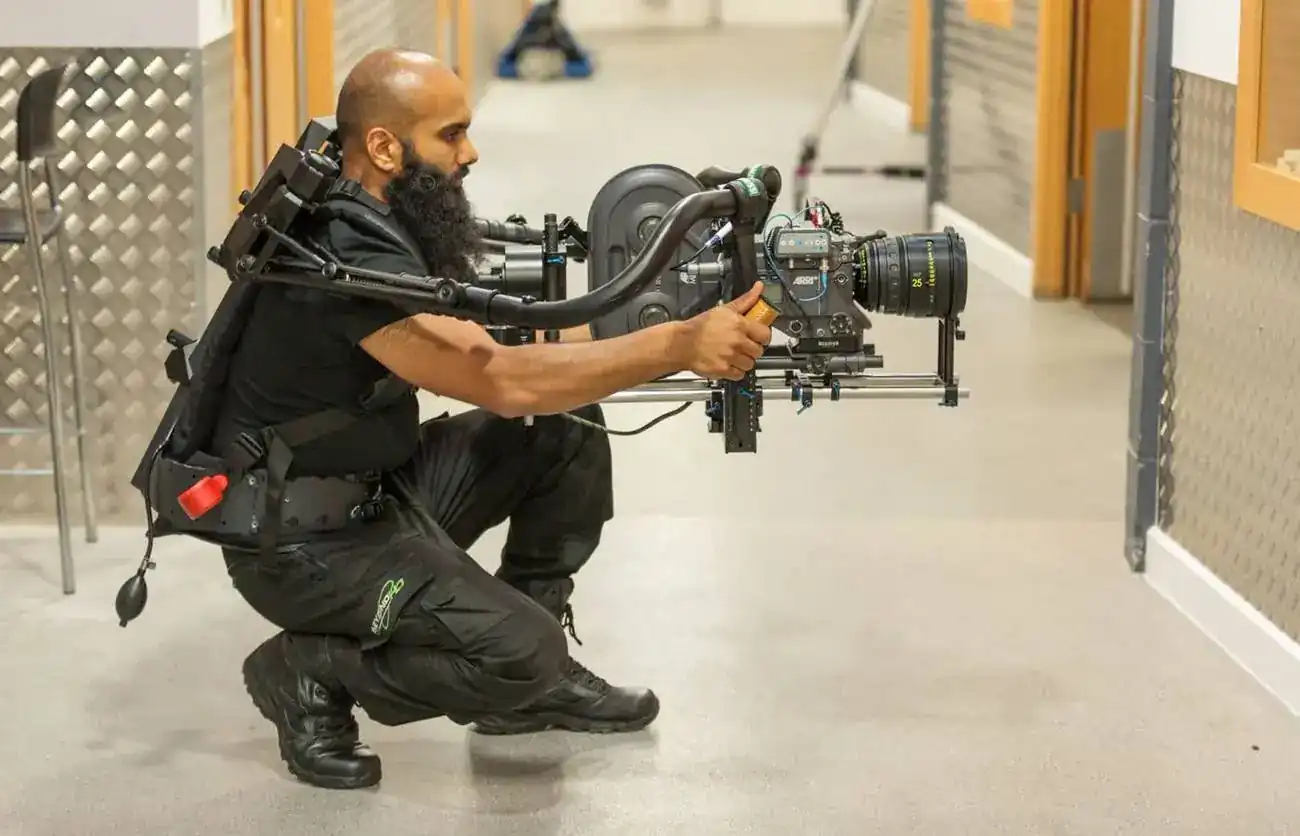 An operator kneeling with a camera on an exoskeleton rig