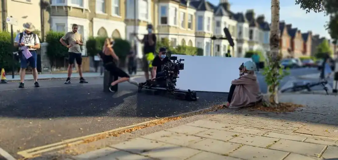 A unit filming on a residential street, the camera on a dolly behind a large bounce board